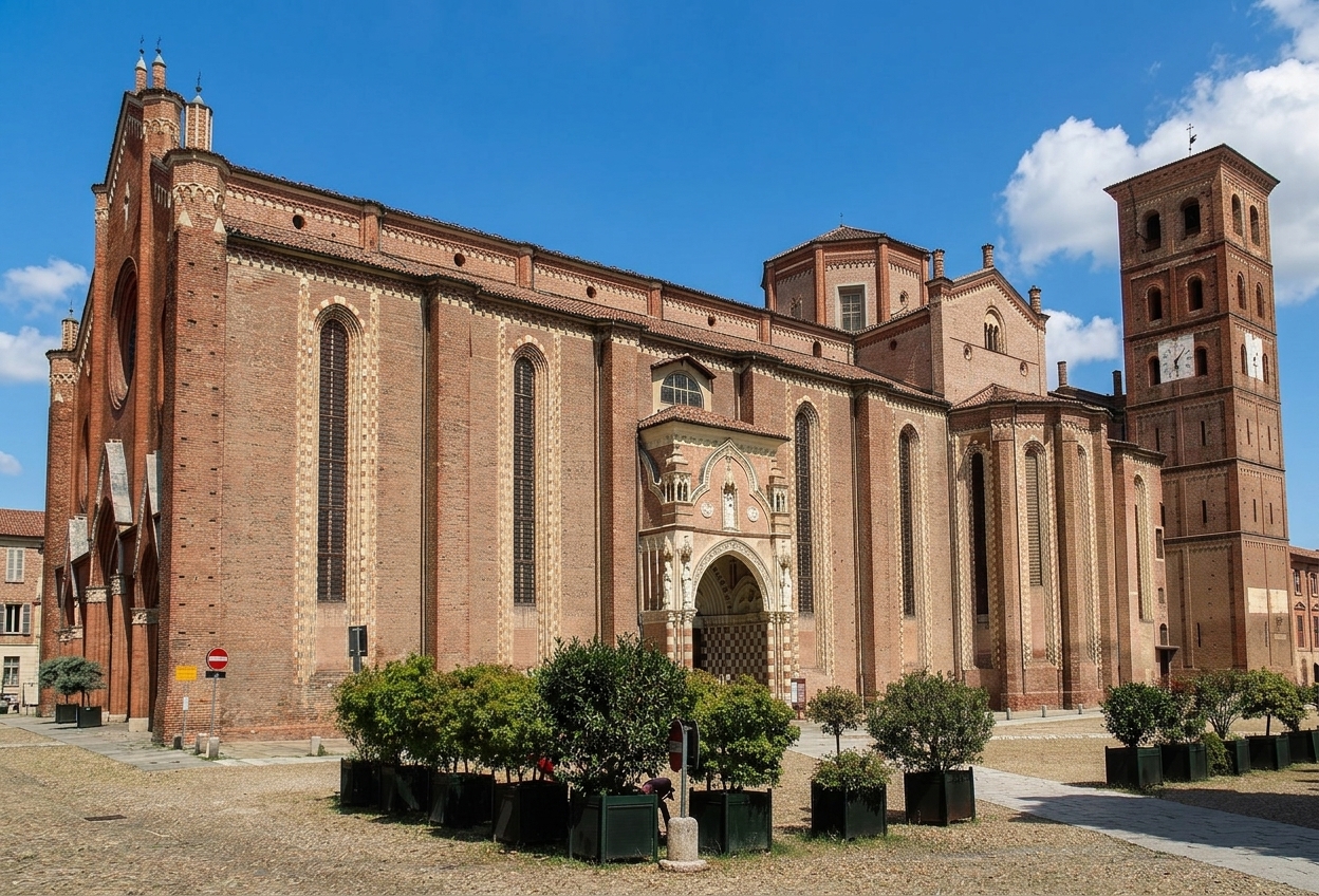 The long brick Gothic flank of Asti cathedral with its carved side portal and square bell tower under a blue sky