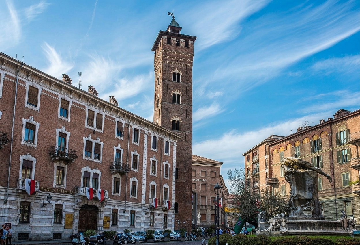 The 13th-century Torre Troyana rising above the palazzi and fountain of Piazza Medici in Asti under a streaked blue sky
