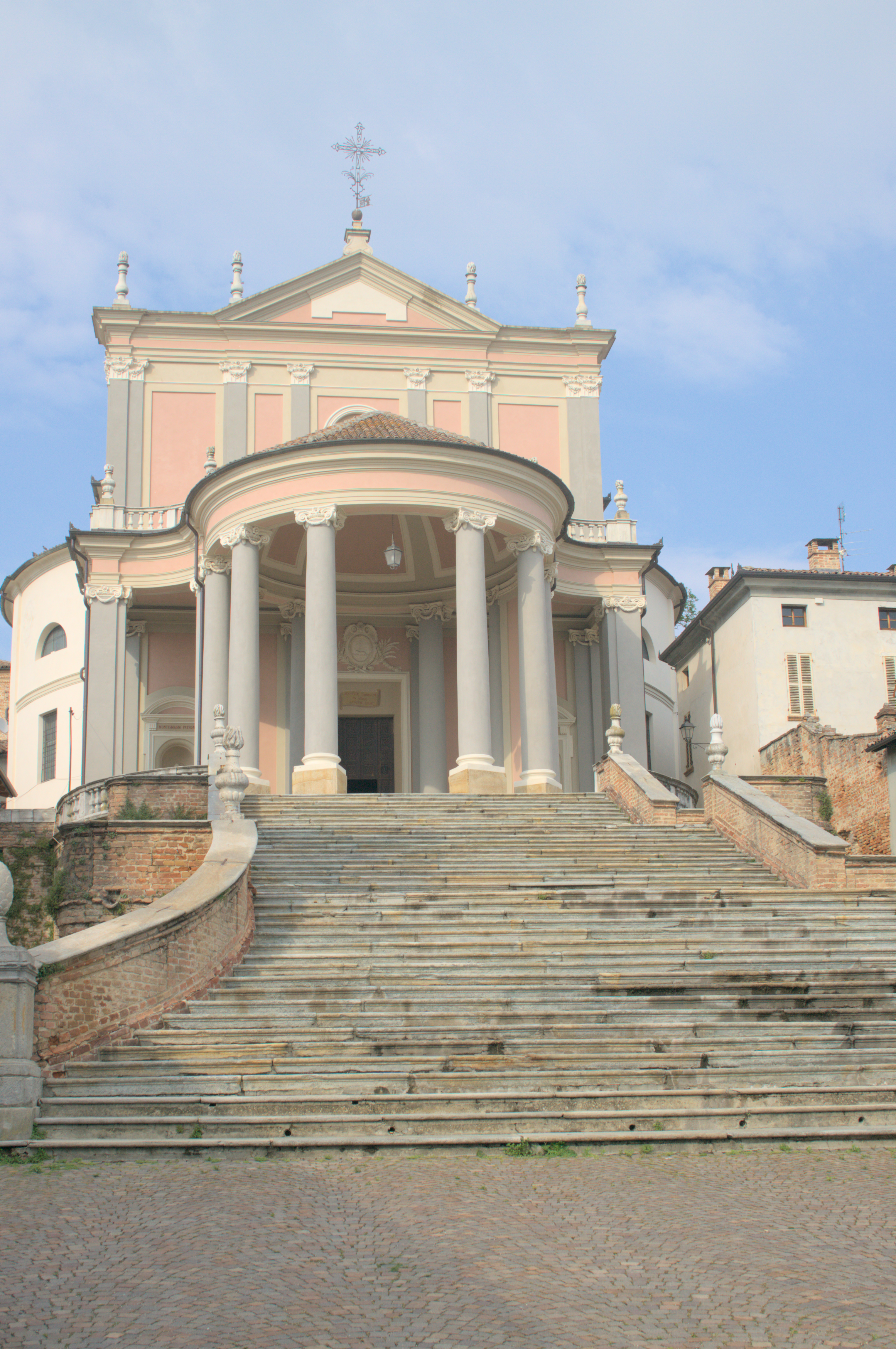 The pink-and-grey Baroque facade of the church of Santi Martino e Stefano in Montemagno, its curved portico at the top of the staircase