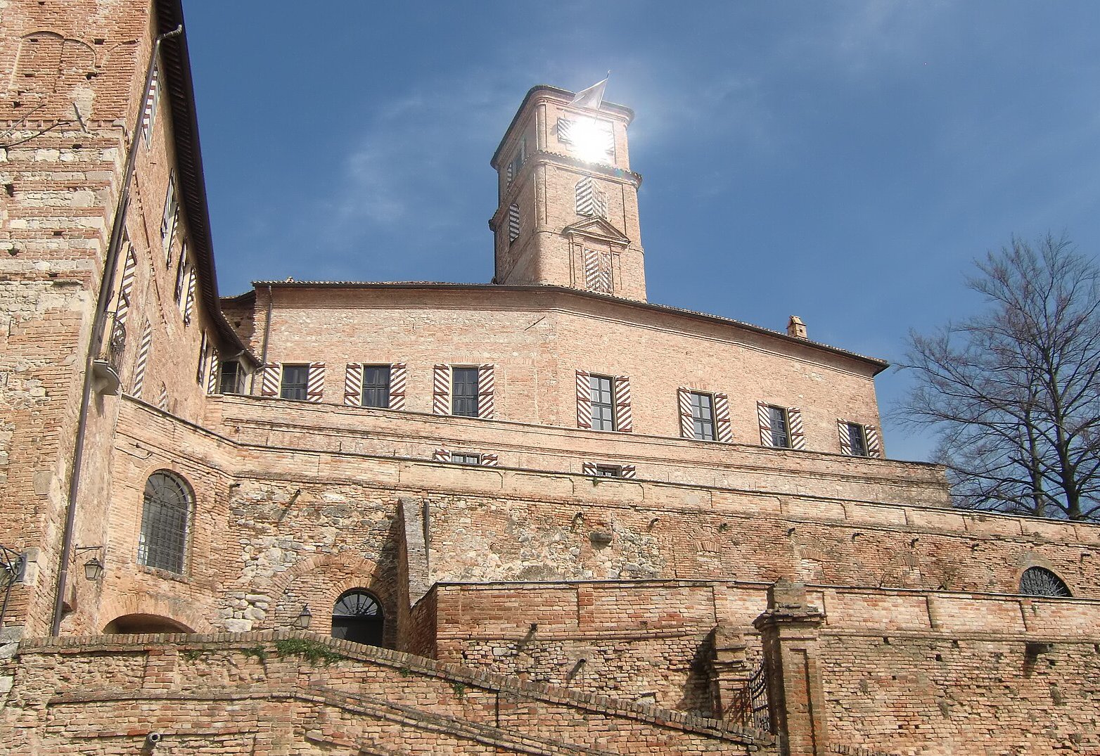 The brick castle of Montiglio on its hilltop, with terraced walls and its square tower against a blue sky