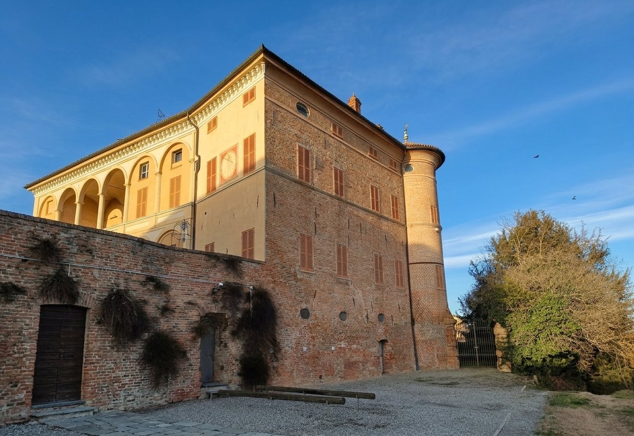 The castle of Rinco, a tall brick block with an ochre loggia wing and a round corner tower, lit by low sun under a blue sky