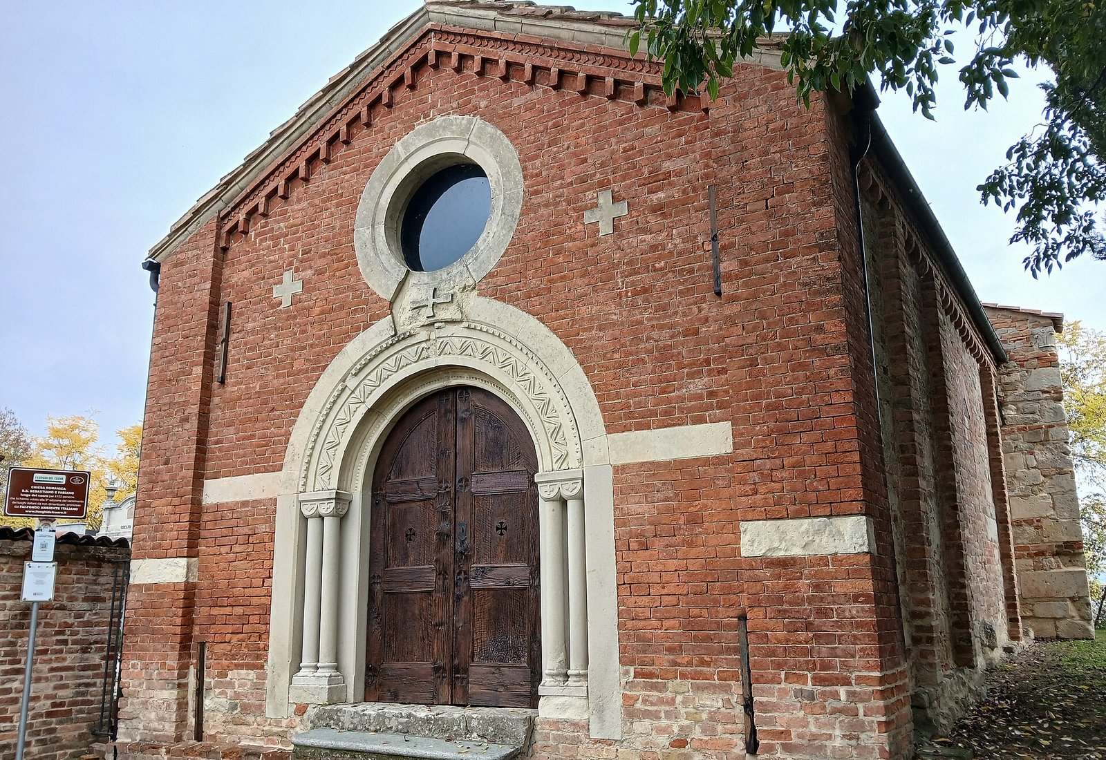 The red-brick gabled front of the Romanesque church of Santi Sebastiano e Fabiano at Scandeluzza, with a round window above a carved arched portal