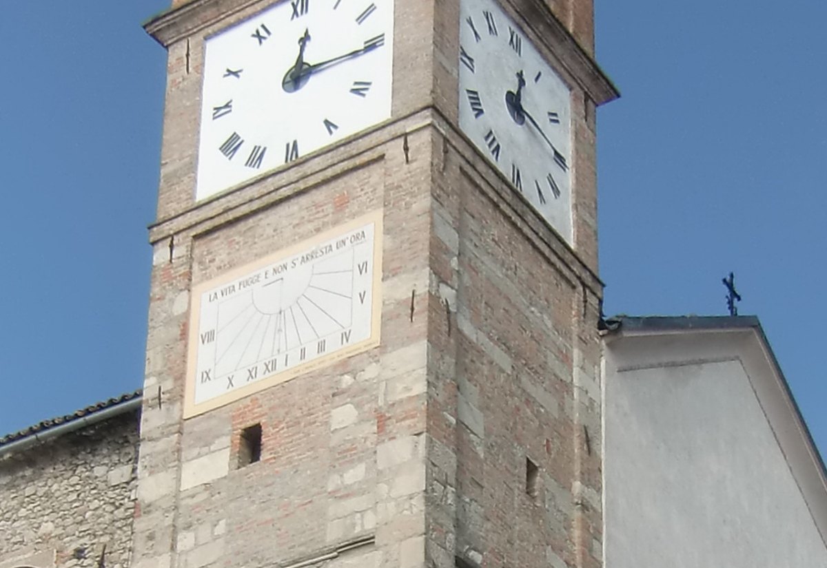 A painted sundial with the motto 'La vita fugge e non s'arresta un'ora' on the stone-and-brick bell tower of Montiglio's parish church, below the clock faces