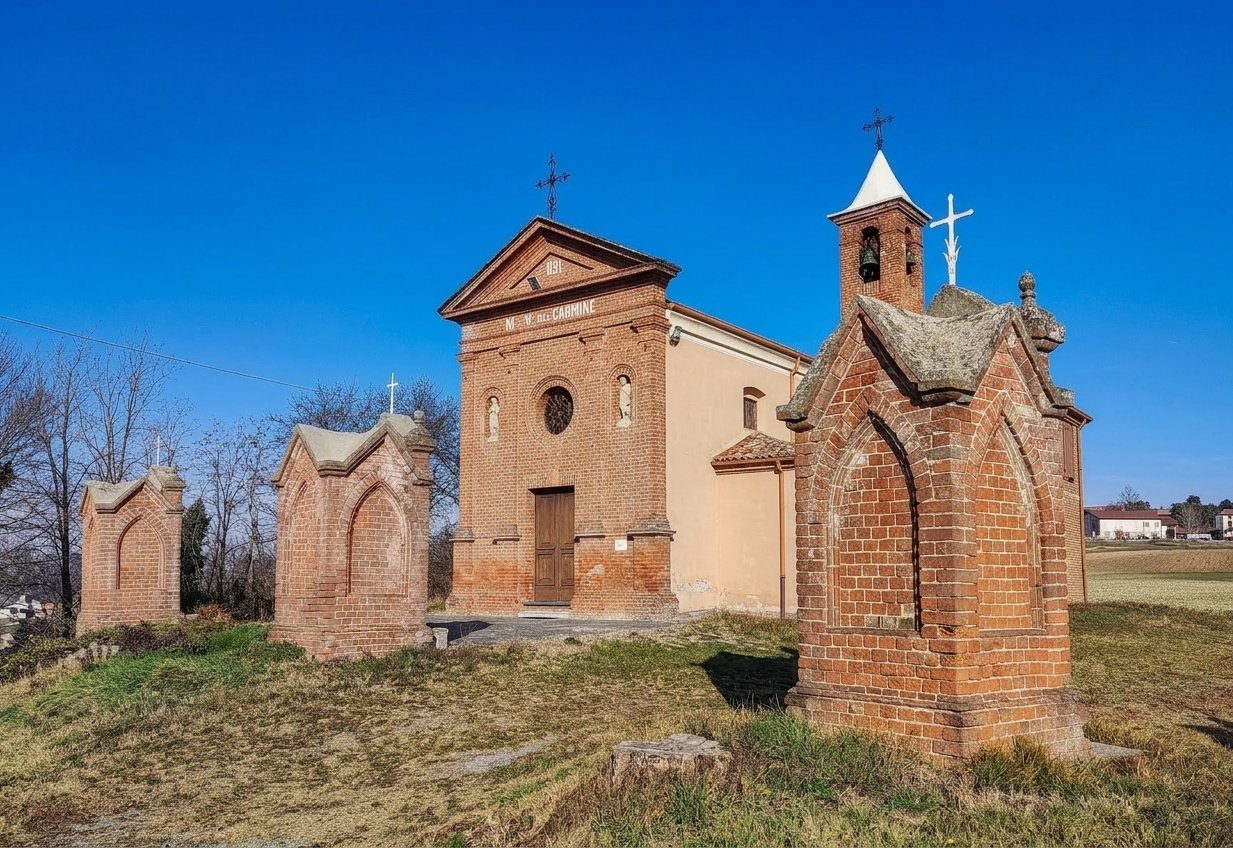 The brick façade of the Madonna del Carmine sanctuary at Albarengo, with its little bell tower and small brick devotional chapels on the grass in front