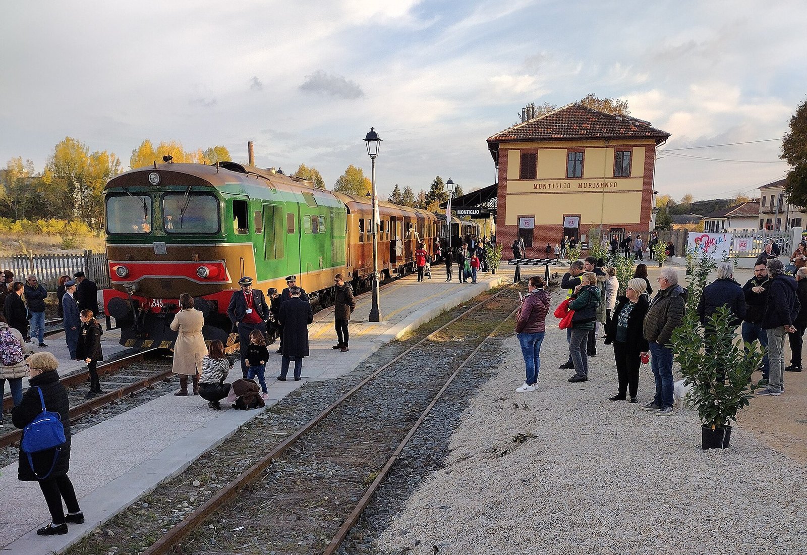 A heritage diesel train and crowds of visitors on the platform of the brick-and-render Montiglio-Murisengo station on an autumn day