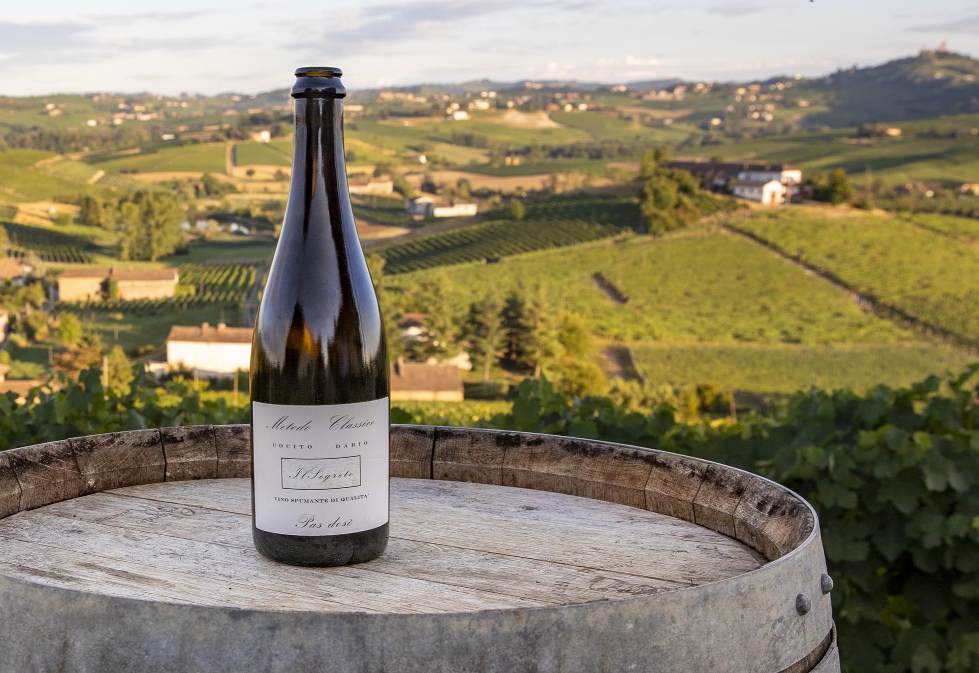 A Cocito Dario metodo classico bottle on a barrel above the vineyards of the Crena hill at Agliano Terme