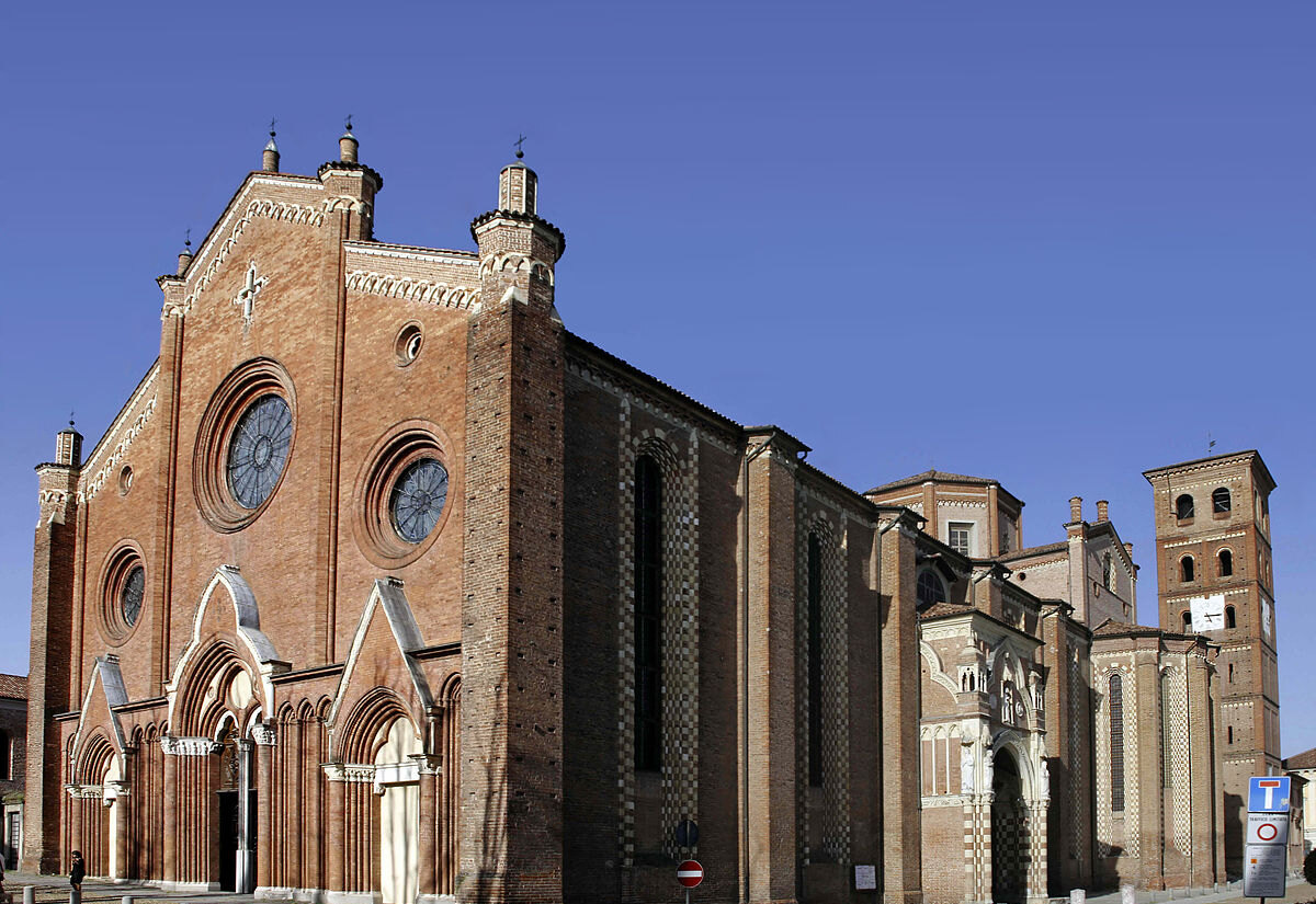 The Gothic brick façade and bell tower of Asti Cathedral under a clear blue sky