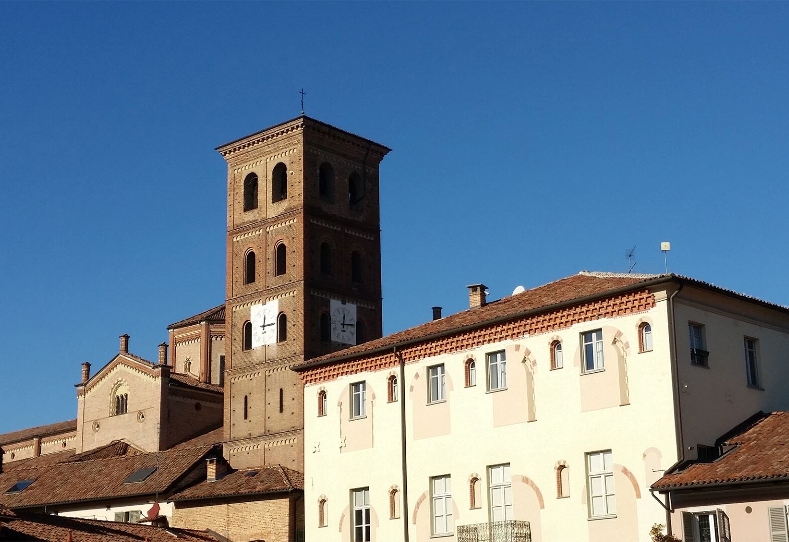 A medieval brick bell tower rising above a pale palazzo and the terracotta roofs of Asti's old town