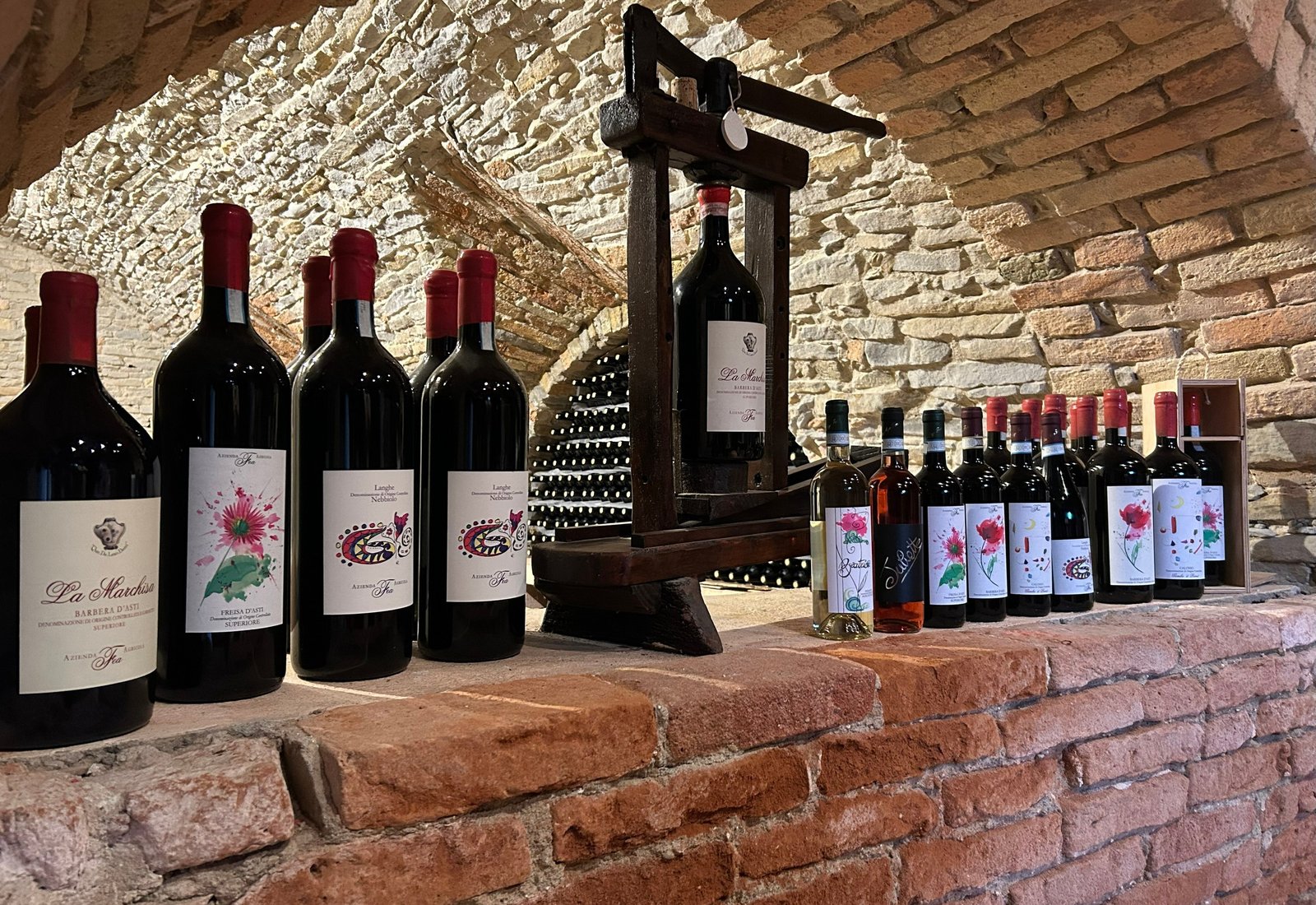 Fea wines lined up on a brick ledge under the stone vault of the winery's underground crotin, with an old wooden press