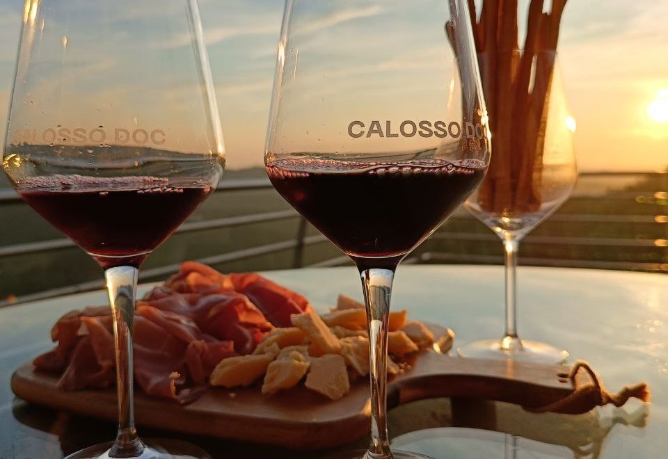 Two glasses of Calosso DOC and a board of prosciutto and cheese on the Cascina Comina terrace at sunset