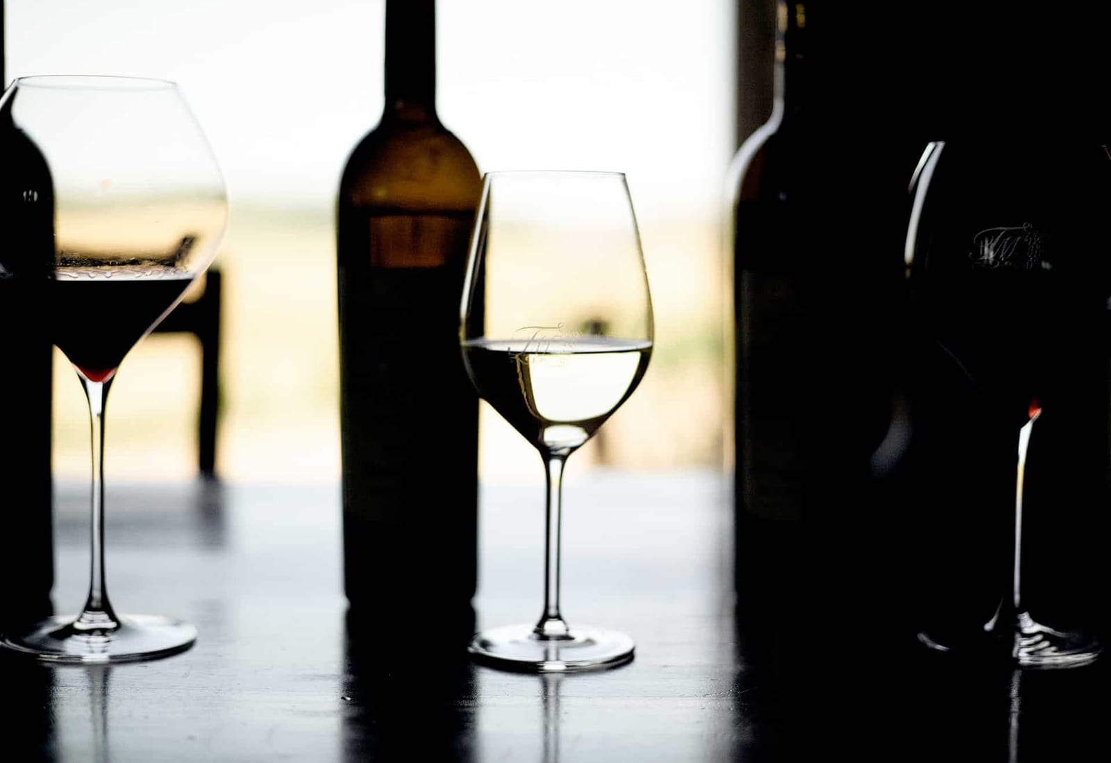 Glasses of red and white wine with bottles and a view over the vineyards at Tenuta Montemagno