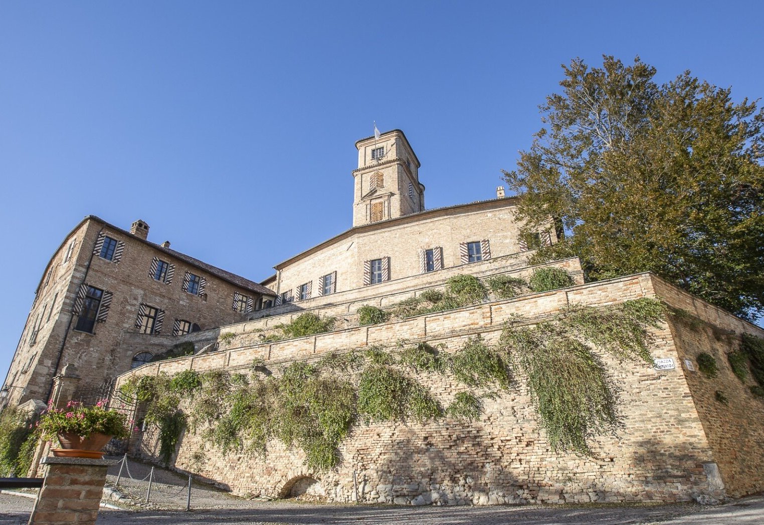 The brick walls and tower of Montiglio castle rising above Piazza Umberto I under a clear blue sky
